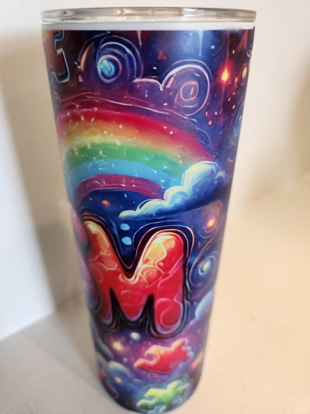 Autistic Pride tumbler - side view showing M letter with rainbow arc on galaxy background