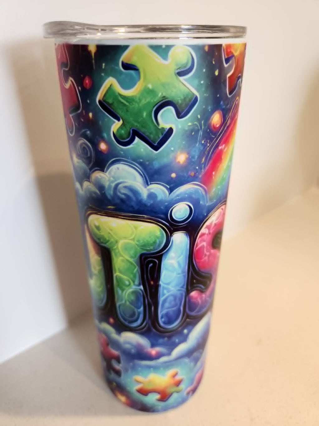 Autistic Pride tumbler - side view showing TIC lettering with green puzzle piece on cosmic background